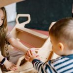 Children enjoying a playful moment with a wooden rocker indoors, emphasizing fun and interaction.